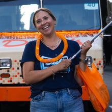 Load image into Gallery viewer, Woman holding a flag, wearing the V-neck Lighting Up the Night T-shirt and an orange light-up necklace, standing in front of the Dick's Drive-In food truck.