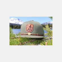 Load image into Gallery viewer, Olive snapback hat w/ tan/brown leather patch w/ Sasquatch carrying DDIR bag. Tan laces & wooden "Dick's" cloud logo clip