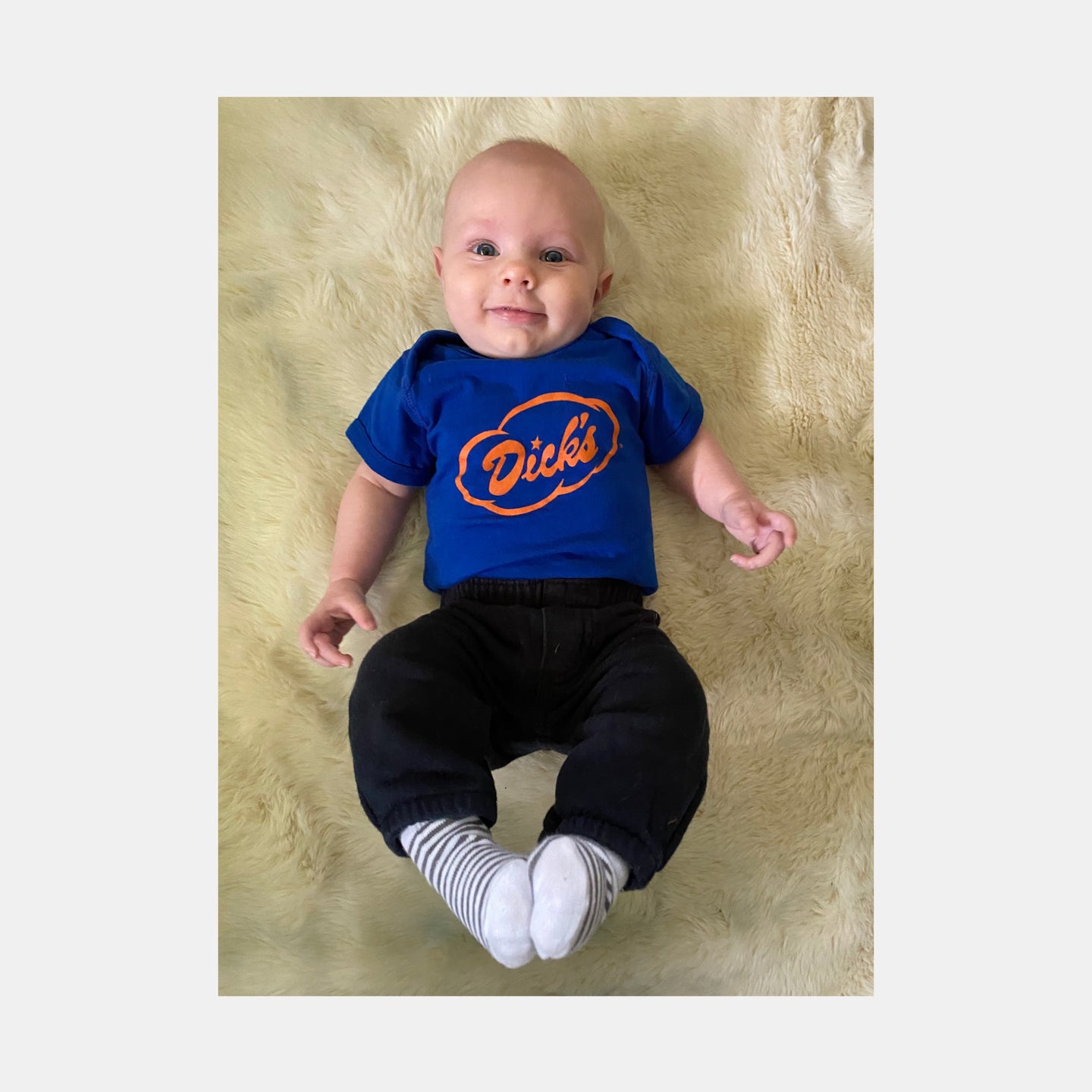 Baby wearing royal blue onesie with Dick's Drive-In orange cloud logo on front and black pants.